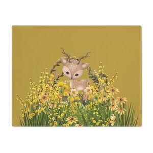 Puede incluir: Un mantel individual rectangular con un ciervo de dibujos animados rodeado de flores amarillas y follaje verde. El ciervo tiene manchas marrones y cuernos, sobre un fondo amarillo mostaza. El diseño es caprichoso y decorativo.