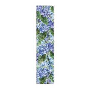 May include: A rectangular table runner featuring a watercolor floral pattern of blue and purple hydrangeas with green leaves. The runner's design is a repeating pattern of the flowers and foliage.