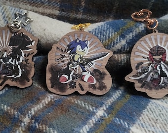 May include: Three wooden keychains featuring characters from the Sonic the Hedgehog video game series. The keychains are painted with a grunge-style background and feature Sonic, Shadow, and a third character.
