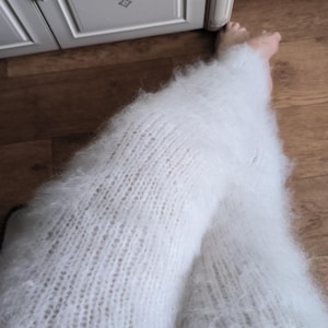 Puede incluir: Un par de calentadores de piernas largos, blancos y difusos, con una textura gruesa tejida a mano. Estos accesorios suaves y de gran altura cubren la parte inferior de las piernas y están hechos de un hilo cepillado y esponjoso.
