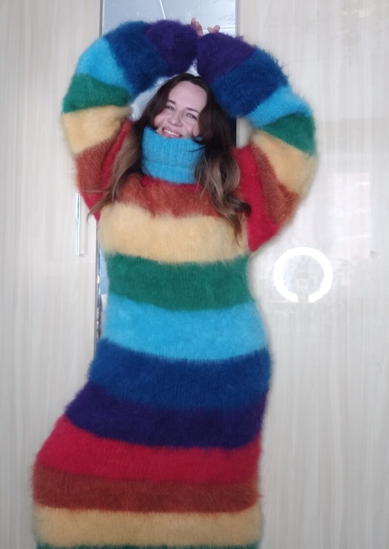 May include: A long, rainbow-striped sweater dress with a turtleneck. The dress features horizontal bands of red, orange, yellow, green, blue, and purple. The sleeves are long and the material appears to be fuzzy.
