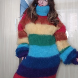 May include: A long, rainbow-striped sweater dress with a high, turquoise turtleneck. The dress features horizontal bands of red, orange, yellow, green, blue, and purple. The sleeves are long and fluffy, matching the soft, textured appearance of the dress.