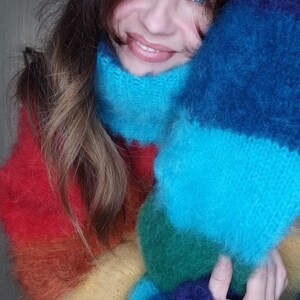May include: A vibrant, rainbow-colored knitted scarf and sweater set. The scarf features a high, cozy collar in shades of blue, while the sweater transitions through red, orange, yellow, green, and blue. The soft, fluffy texture adds to the warmth and visual appeal.