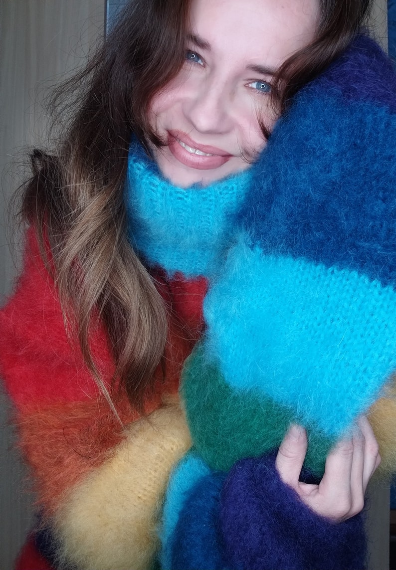 May include: A vibrant, rainbow-colored knitted scarf and sweater set. The scarf features a high, cozy collar in shades of blue, while the sweater transitions through red, orange, yellow, green, and blue. The soft, fluffy texture adds to the warmth and visual appeal.