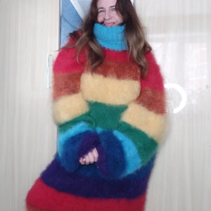 May include: A long, oversized rainbow-striped sweater with a high, turquoise turtleneck. The sweater features horizontal bands of red, orange, yellow, green, blue, and purple. The sleeves are long and the material appears soft and fuzzy.