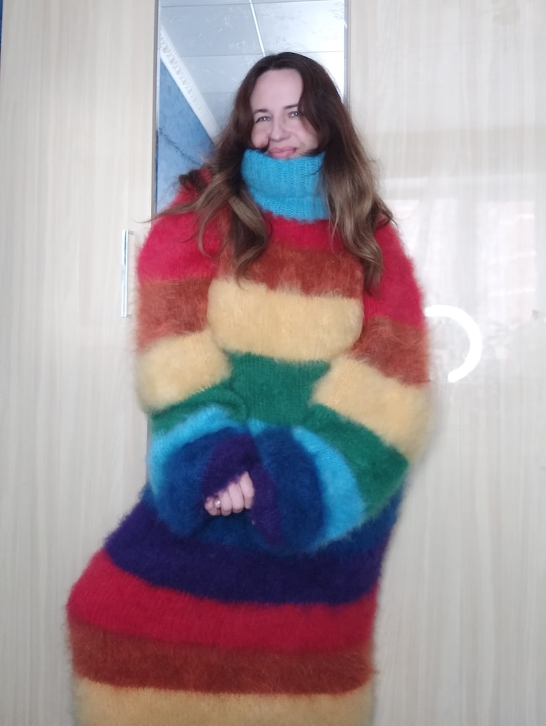 May include: A long, oversized rainbow-striped sweater with a high, turquoise turtleneck. The sweater features horizontal bands of red, orange, yellow, green, blue, and purple. The sleeves are long and the material appears soft and fuzzy.