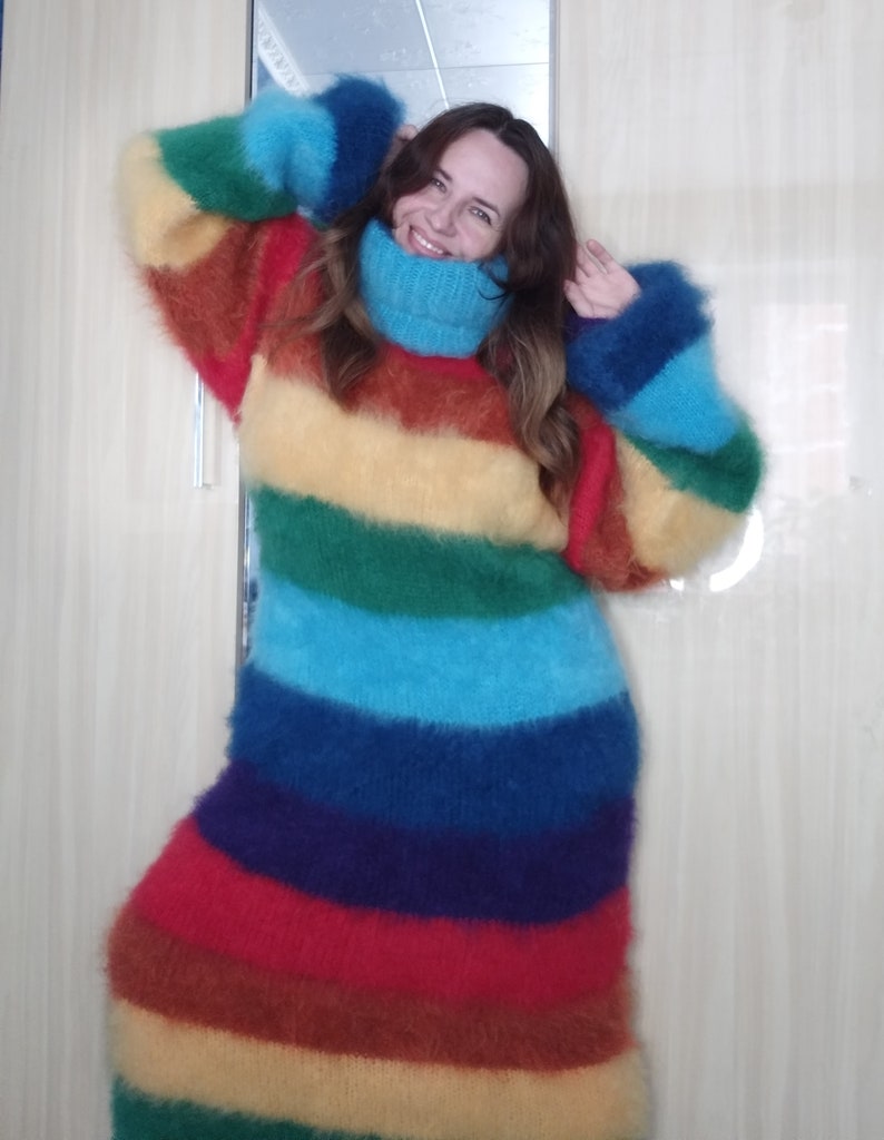 May include: A long, rainbow-striped sweater with a high turtleneck and long sleeves. The sweater features bands of red, orange, yellow, green, blue, and purple. The fluffy knitwear is a cozy and colorful garment.