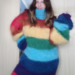 May include: A long-sleeved, rainbow-striped sweater with a turtleneck. The sweater features bands of red, orange, yellow, green, blue, and purple. The sleeves are long and puffy, and the sweater appears to be made of a soft, fuzzy material.