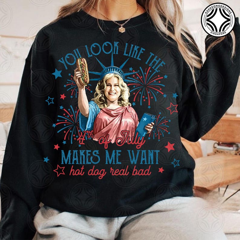 May include: Black sweatshirt with a graphic of a woman dressed as the Statue of Liberty holding a hot dog and a book. Text reads "You look like the 4th of July makes me want hot dog real bad."