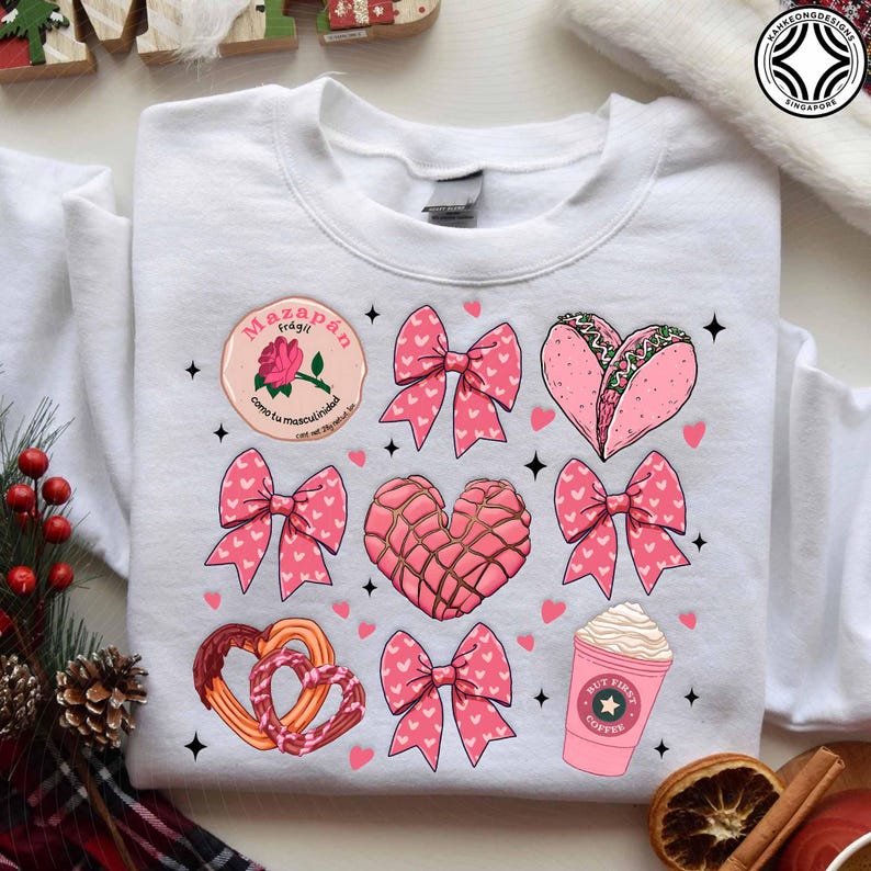 May include: White sweatshirt featuring a variety of pink graphics, including bows, hearts, a taco, a coffee cup, and a concha. The sweatshirt also has a circular graphic with text and a rose. Small black star shapes are scattered around the design.