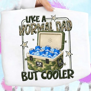 May include: White t-shirt with a graphic of a camouflage cooler filled with blue cans and ice. The text reads "LIKE A NORMAL DAD BUT COOLER" in green and camouflage lettering, with star accents.