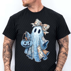 May include: A black t-shirt featuring a graphic of a light blue ghost wearing a large floral patterned bow on its head. The ghost is holding a blue pumpkin-shaped bucket. The ghost's body is decorated with various blue and tan floral fabric patches.