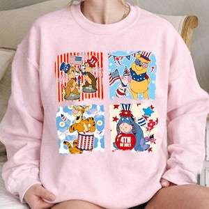 May include: Pale pink sweatshirt with four square designs featuring Disney characters celebrating the 4th of July. Chip and Dale, Winnie the Pooh, Tigger, and Eeyore are shown with patriotic themes.