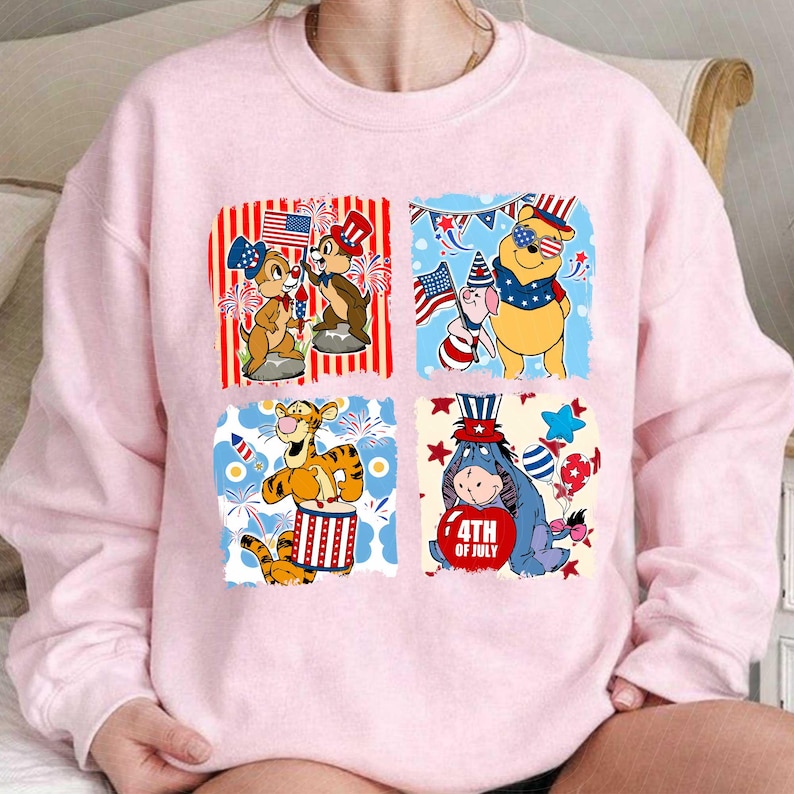 May include: Pale pink sweatshirt with four square designs featuring Disney characters celebrating the 4th of July. Chip and Dale, Winnie the Pooh, Tigger, and Eeyore are shown with patriotic themes.