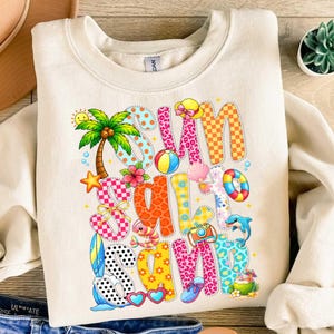 May include: Cream-colored sweatshirt with a colorful "Summer Camp" graphic. The design includes a palm tree, beach ball, starfish, and other summer-themed illustrations. The letters are in various patterns and colors.