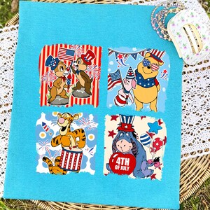 May include: A light blue square fabric with four square images of Disney characters celebrating the 4th of July. Chip and Dale, Winnie the Pooh and Piglet, Tigger, and Eeyore are depicted with patriotic themes.