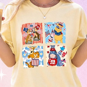 May include: A pale yellow t-shirt with four square designs featuring cartoon characters in patriotic themes. Chip and Dale, Winnie the Pooh, Piglet, Tigger, and Eeyore are shown with American flag and 4th of July motifs.