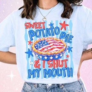 May include: Light blue t-shirt with a graphic of a sweet potato pie decorated with the American flag. The text on the shirt reads "Sweet Potato Pie & I Shut My Mouth" in red and blue.