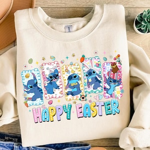 Puede incluir: Sudadera de color crema con un gráfico colorido del personaje Stitch en diseños temáticos de Pascua. El gráfico incluye el texto "HAPPY EASTER" en una fuente lúdica, con colores pastel y elementos decorativos.