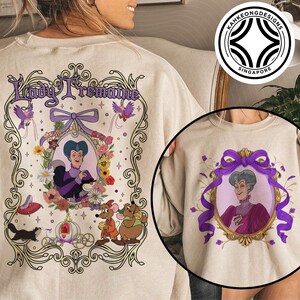 Puede incluir: Sudadera beige con una ilustraci&oacute;n enmarcada de Lady Tremaine. El dise&ntilde;o incluye un retrato, detalles florales y el texto "Lady Tremaine". Una versi&oacute;n m&aacute;s peque&ntilde;a del dise&ntilde;o est&aacute; en la manga.