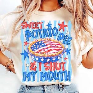 May include: Cream-colored t-shirt with a patriotic design. The graphic features a sweet potato pie with an American flag design, surrounded by stars and the text "Sweet Potato Pie & I Shut My Mouth" in red and blue.