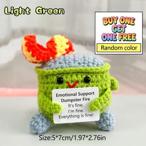 May include: A light green crocheted emotional support dumpster fire toy with a red and yellow flame. The toy has a smiling face and holds a sign that reads "Emotional Support Dumpster Fire. It's fine, I'm fine. Everything is fine!" Measures 1.97" x 2.76".