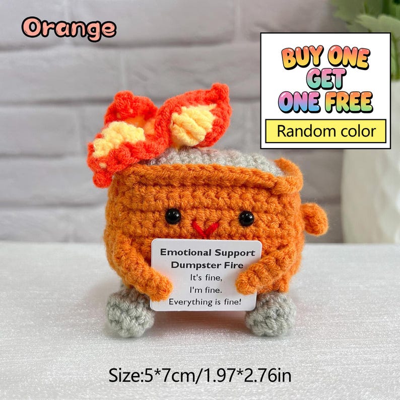 May include: An orange crocheted dumpster fire with a gray top and feet, holding a sign that reads "Emotional Support Dumpster Fire. It's fine, I'm fine. Everything is fine!" The item is 1.97" x 2.76" in size.