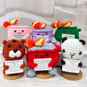 May include: Five crocheted stuffed animals, each representing a different animal and holding a sign with a message of encouragement. The animals are a tiger, a panda, a dumpster fire, and two others. The signs are all white with black text.