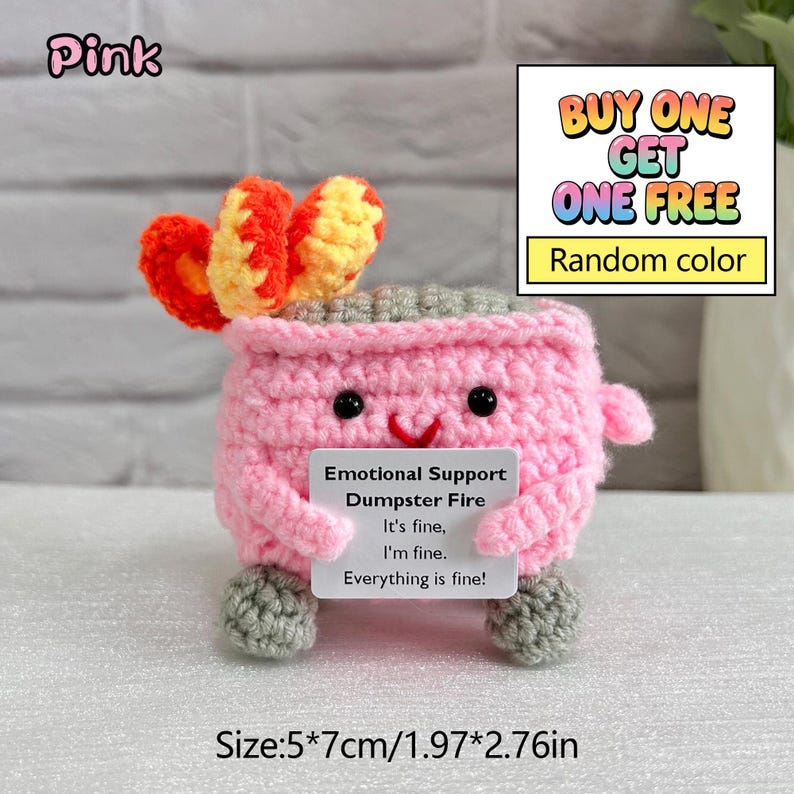 May include: A pink crocheted succulent plant with orange and yellow accents, featuring a smiling face and gray feet. It holds a sign that reads "Emotional Support Dumpster Fire." The item measures 1.97 x 2.76 inches. The image also includes the text "BUY ONE GET ONE FREE."
