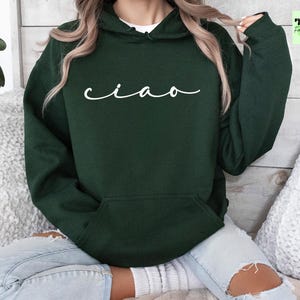K&ouml;nnte beinhalten: Ein dunkelgr&uuml;ner Kapuzenpullover mit dem Wort "ciao" in wei&szlig;er Kursivschrift auf der Vorderseite.