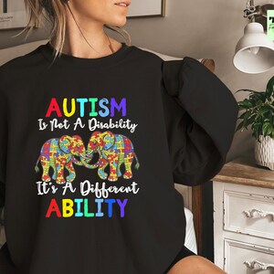 May include: Black sweatshirt with a colorful graphic of two elephants made of puzzle pieces. The text reads "Autism is not a disability, it's a different ability."