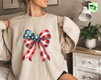 May include: A beige sweatshirt with a large red, white, and blue bow printed on the front. The bow is designed to look like the American flag.