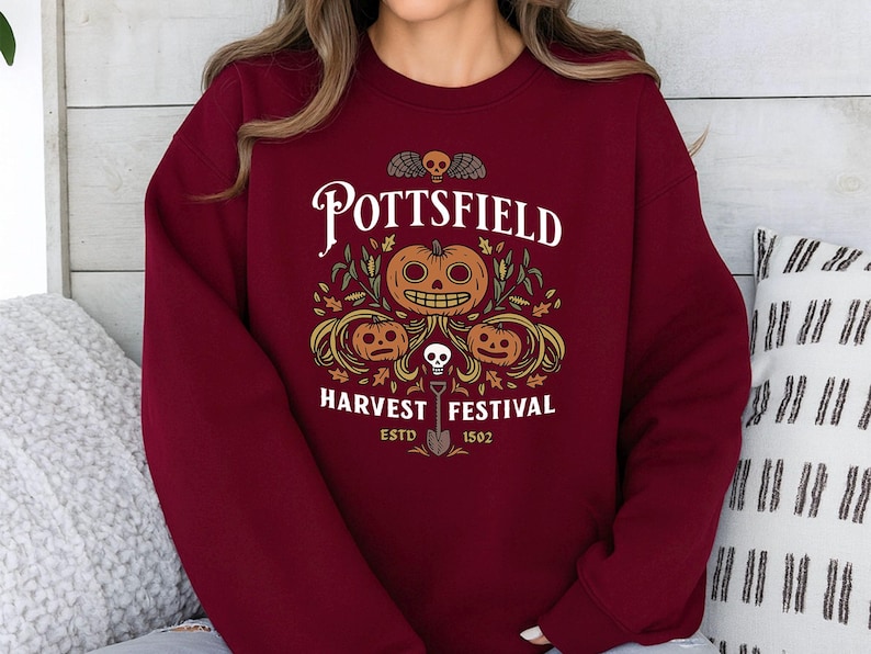 May include: A maroon crewneck sweatshirt featuring a graphic print with the text POTTSFIELD HARVEST FESTIVAL ESTD 1502. The design includes three orange jack-o'-lanterns, green foliage, a small skull, and a shovel centered below the pumpkins.