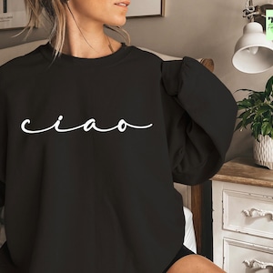 K&ouml;nnte beinhalten: Schwarzer Pullover mit dem Wort "ciao" in wei&szlig;er Kursivschrift.