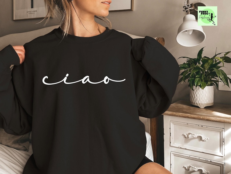 K&ouml;nnte beinhalten: Schwarzer Pullover mit dem Wort "ciao" in wei&szlig;er Kursivschrift.