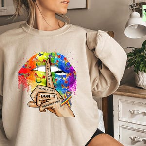 May include: A beige sweatshirt with a rainbow lips design and the text "What you don't understand" and a finger over the lips. The design also includes a rainbow ribbon.