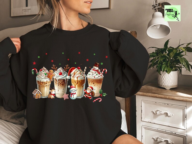 May include: Black sweatshirt featuring a festive design of five holiday-themed coffee drinks with whipped cream, candy canes, and gingerbread men. Red and green star and dot accents complete the holiday theme.