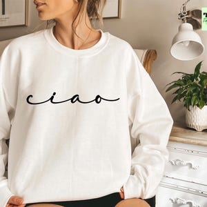 K&ouml;nnte beinhalten: Wei&szlig;er Pullover mit dem Wort "ciao" in schwarzer Kursivschrift.