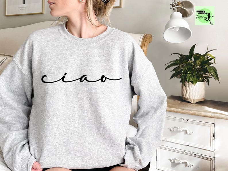 K&ouml;nnte beinhalten: Ein grauer Pullover mit dem Wort "ciao" in schwarzer Kursivschrift.