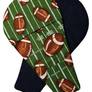 May include: A pair of fabric oven mitts featuring a green football field pattern with brown footballs and white yard line markings. The text 10 and 20 is visible on the field. The reverse side of the mitts is a solid dark navy blue fabric.