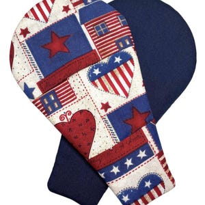 May include: A pair of oven mitts with a patriotic theme. One mitt features a cream-colored fabric with a patchwork pattern of red stars, blue squares, striped hearts, and small houses. The other mitt is a solid dark navy blue fabric on the exterior.