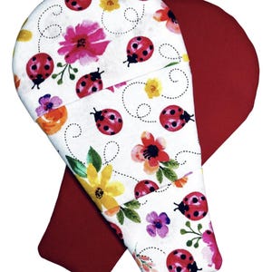 May include: Two oven mitts, one featuring a white background with a pattern of red ladybugs, yellow flowers, and pink blossoms, and the other a solid deep red color. The mitts are shaped with a rounded top and a straight handle section.