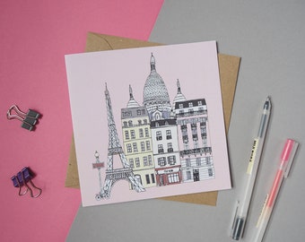 May include: A pink card with a black and white illustration of the Eiffel Tower and other Parisian buildings. The card is on a brown envelope.