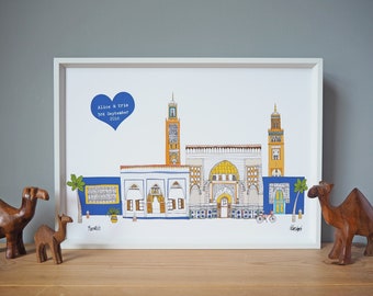 May include: A white framed print with a blue heart that says "Alice & Kris 3rd September 2016". The print features a colorful illustration of a mosque with two minarets, palm trees, and bicycles. The print is on a wooden surface with two wooden camel figurines.