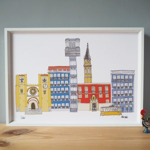 May include: A framed illustration of a cityscape with colorful buildings, including a cathedral, a tower, and a tram. The illustration is in a white frame and is on a wooden surface.