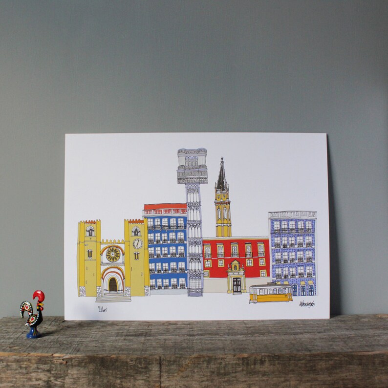 May include: A colorful illustration of Lisbon, Portugal, featuring iconic buildings like the Jer&oacute;nimos Monastery, the Bel&eacute;m Tower, and the Santa Justa Lift. The illustration is printed on white paper and framed with a white border.