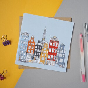 May include: A blue card with a drawing of colorful buildings in a row. The buildings have different styles and colors, including yellow, orange, red, and blue. There are two bicycles in front of the buildings.