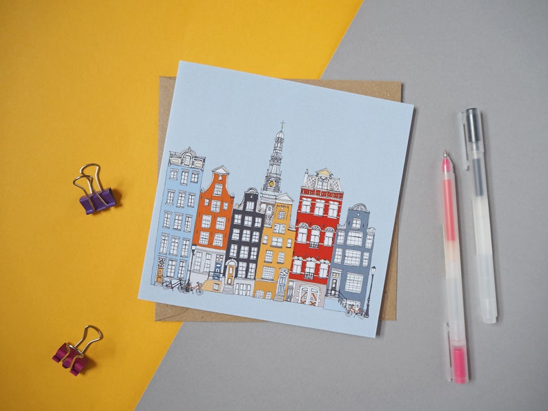 May include: A blue card with a drawing of colorful buildings in a row. The buildings have different styles and colors, including yellow, orange, red, and blue. There are two bicycles in front of the buildings.