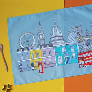 May include: A blue tea towel with a colorful illustration of London landmarks, including Big Ben, the London Eye, and a red double-decker bus.