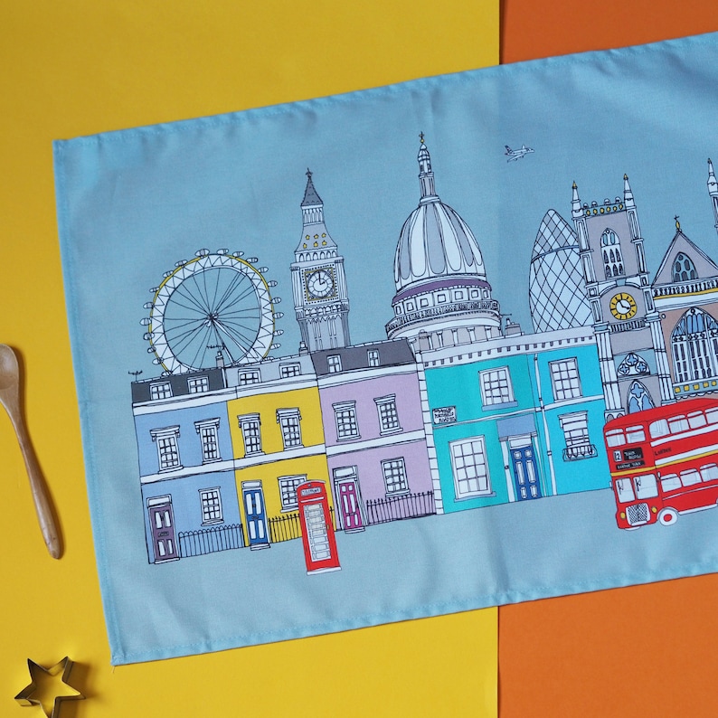 May include: A blue tea towel with a colorful illustration of London landmarks, including Big Ben, the London Eye, and a red double-decker bus.